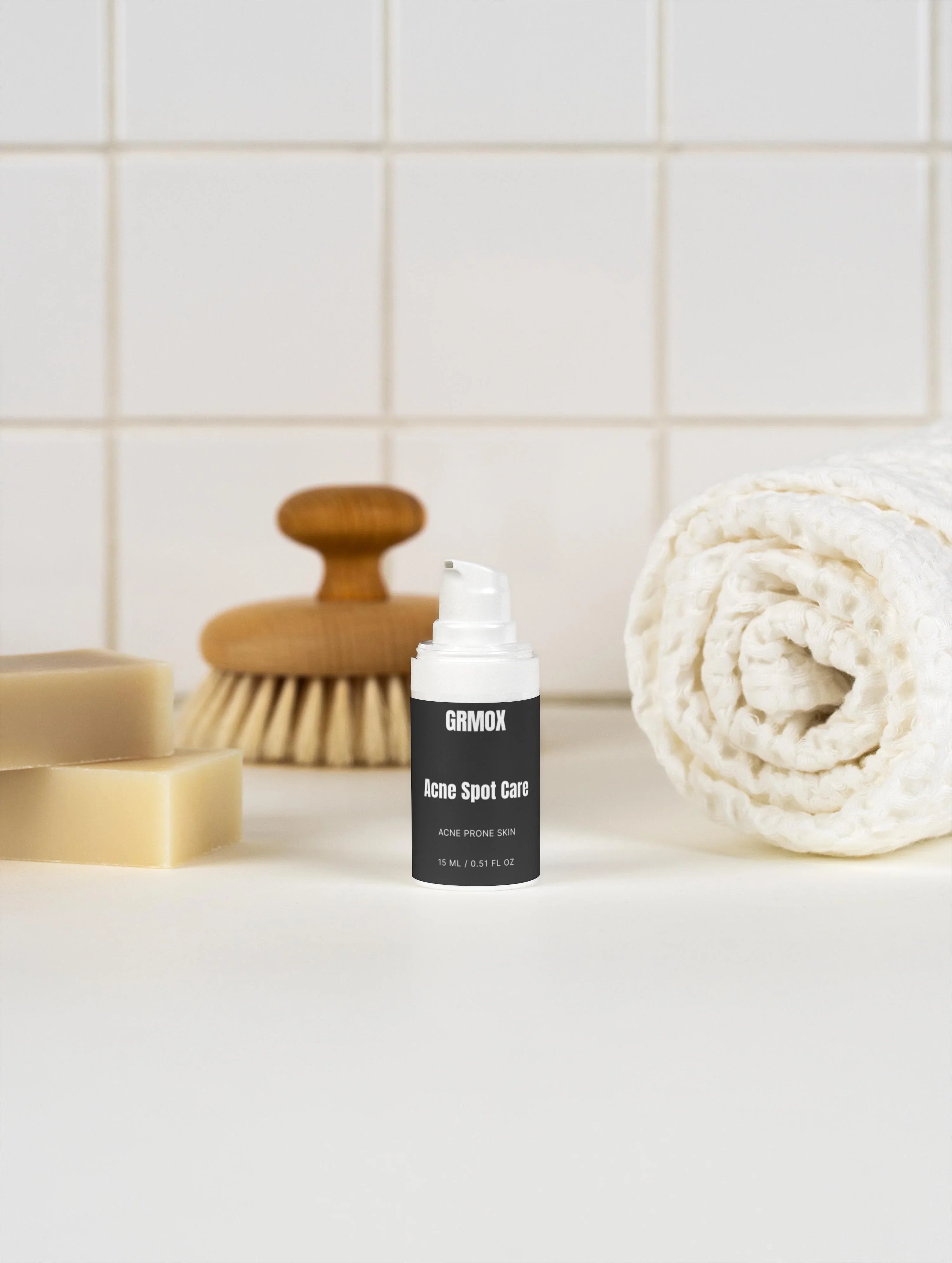 GRMOX Acne Spot Care for acne prone skin, 15ml bottle with pump, beside soap, brush, and towel on white tiles