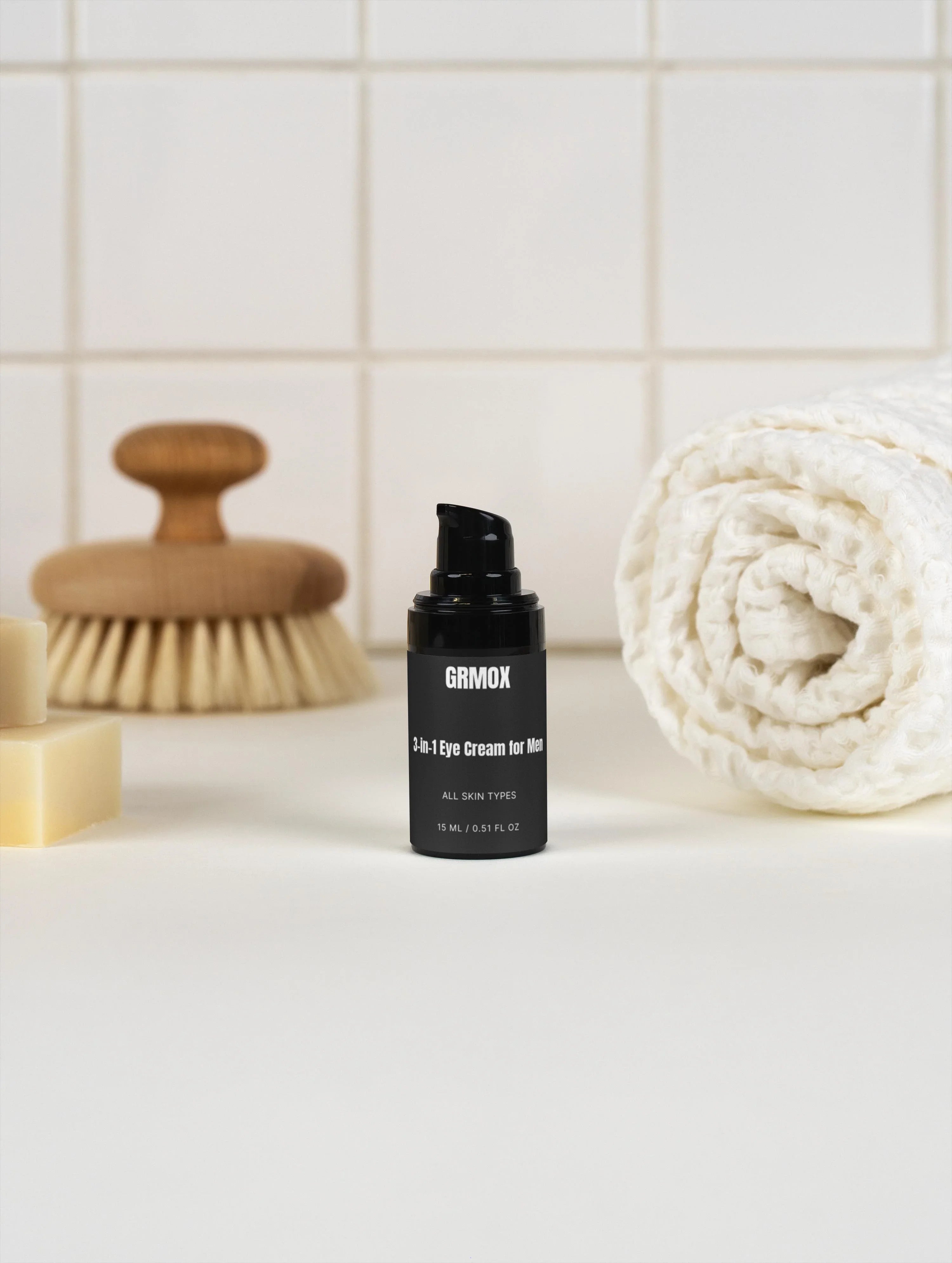 GRMOX 3-in-1 Eye Cream for Men, all skin types, 15ml bottle on bathroom counter with towel and brush