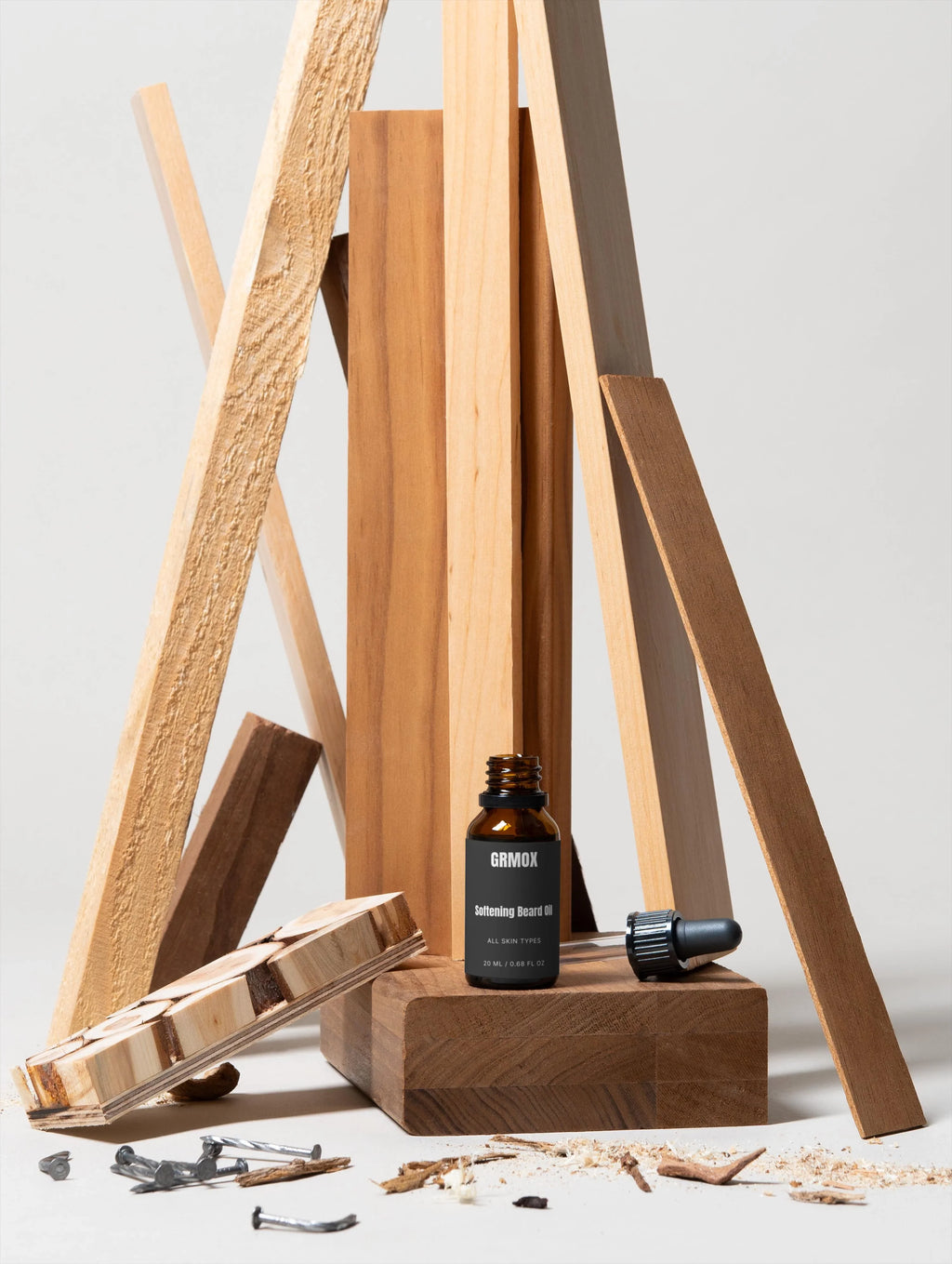 GRMOX Softening Beard Oil bottle with dropper, displayed on wood blocks amid sawdust and nails, for all skin types.