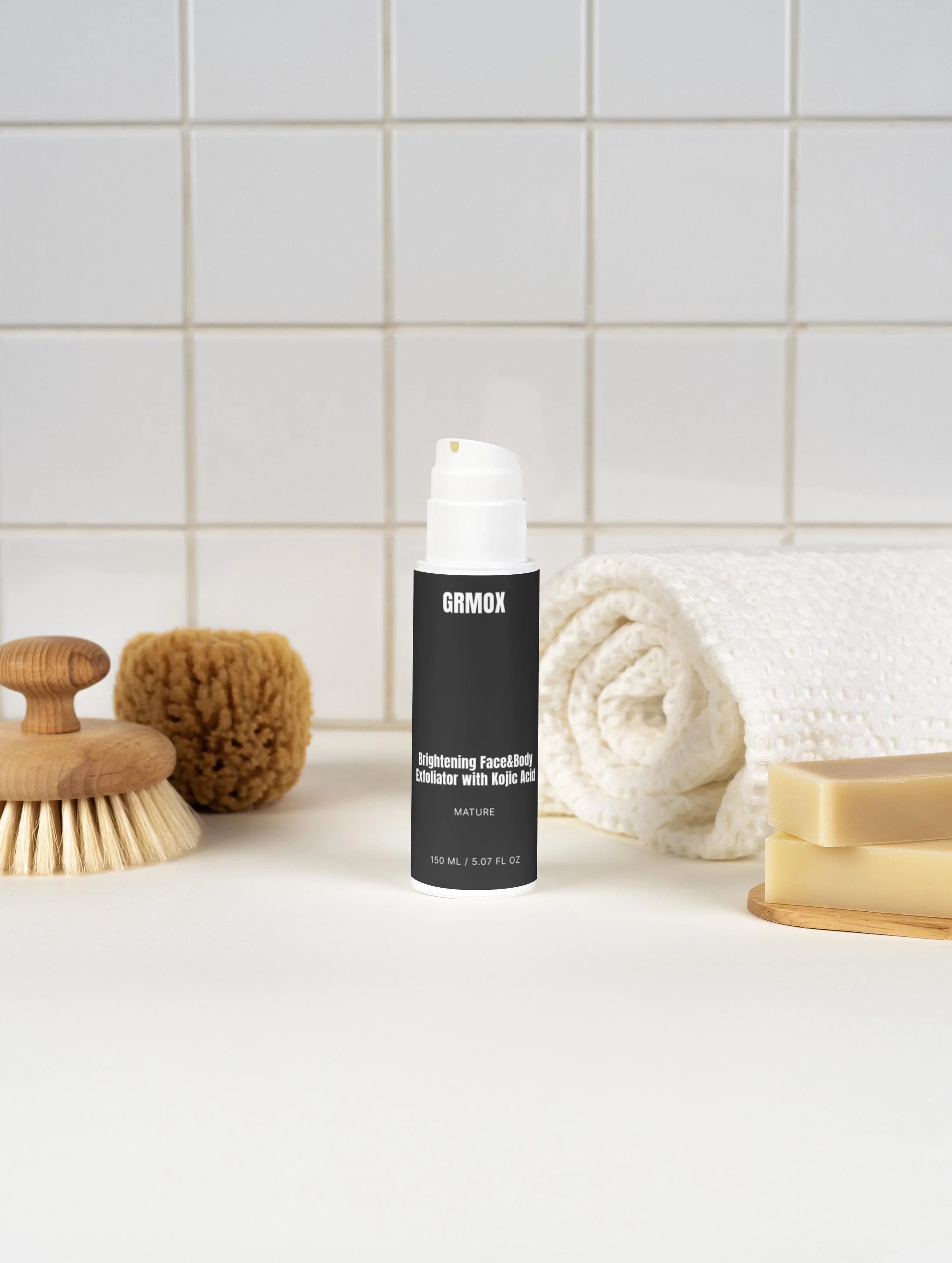 Brightening face and body exfoliator with kojic acid in bathroom setting with towel, brush, and soap