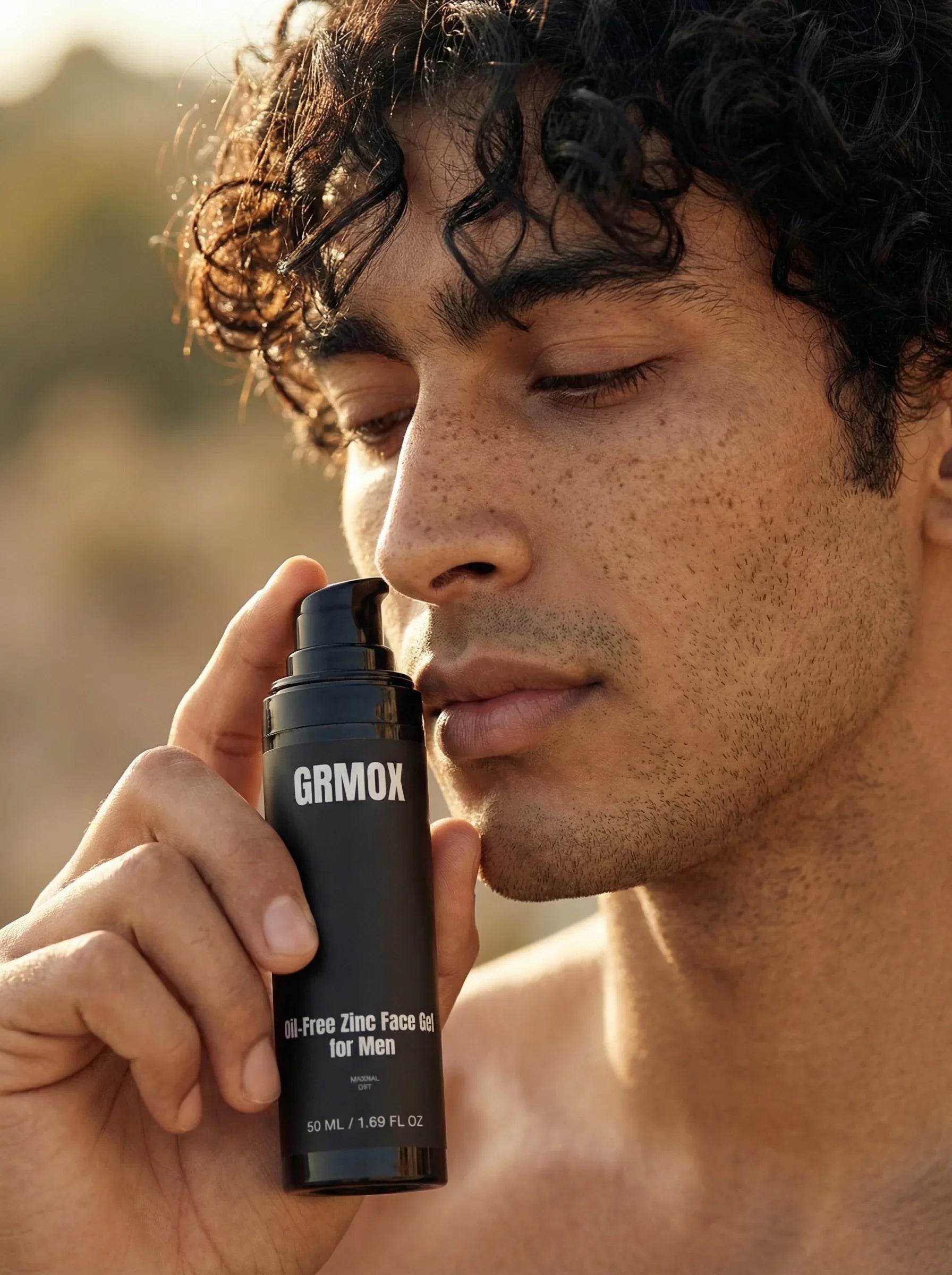 Man holding GRMOX Oil-Free Zinc Face Gel for Men, natural outdoor lighting, curly hair, freckled skin