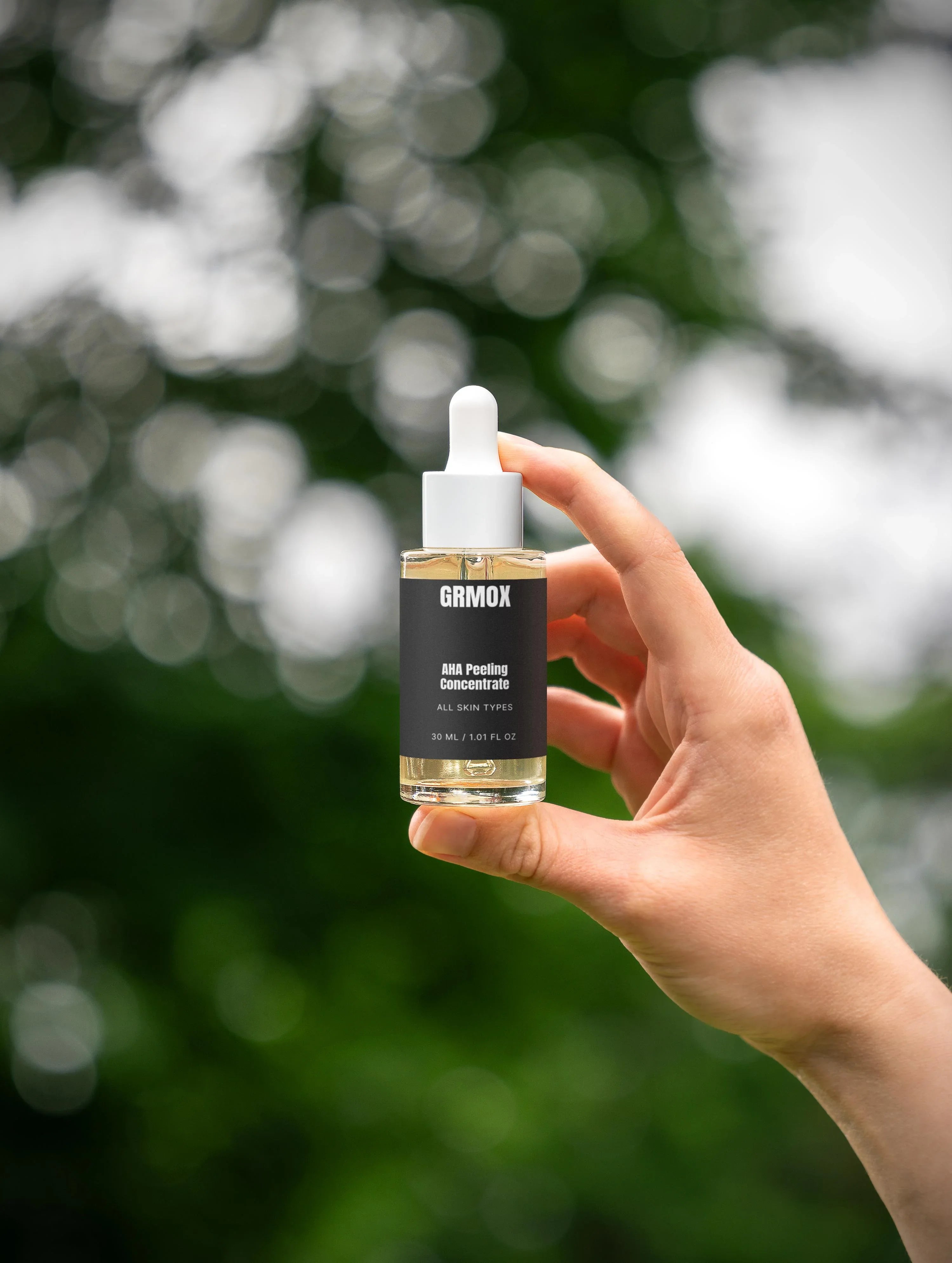 Hand holding GRMOX AHA Peeling Concentrate serum for all skin types, 30ml, against green bokeh background