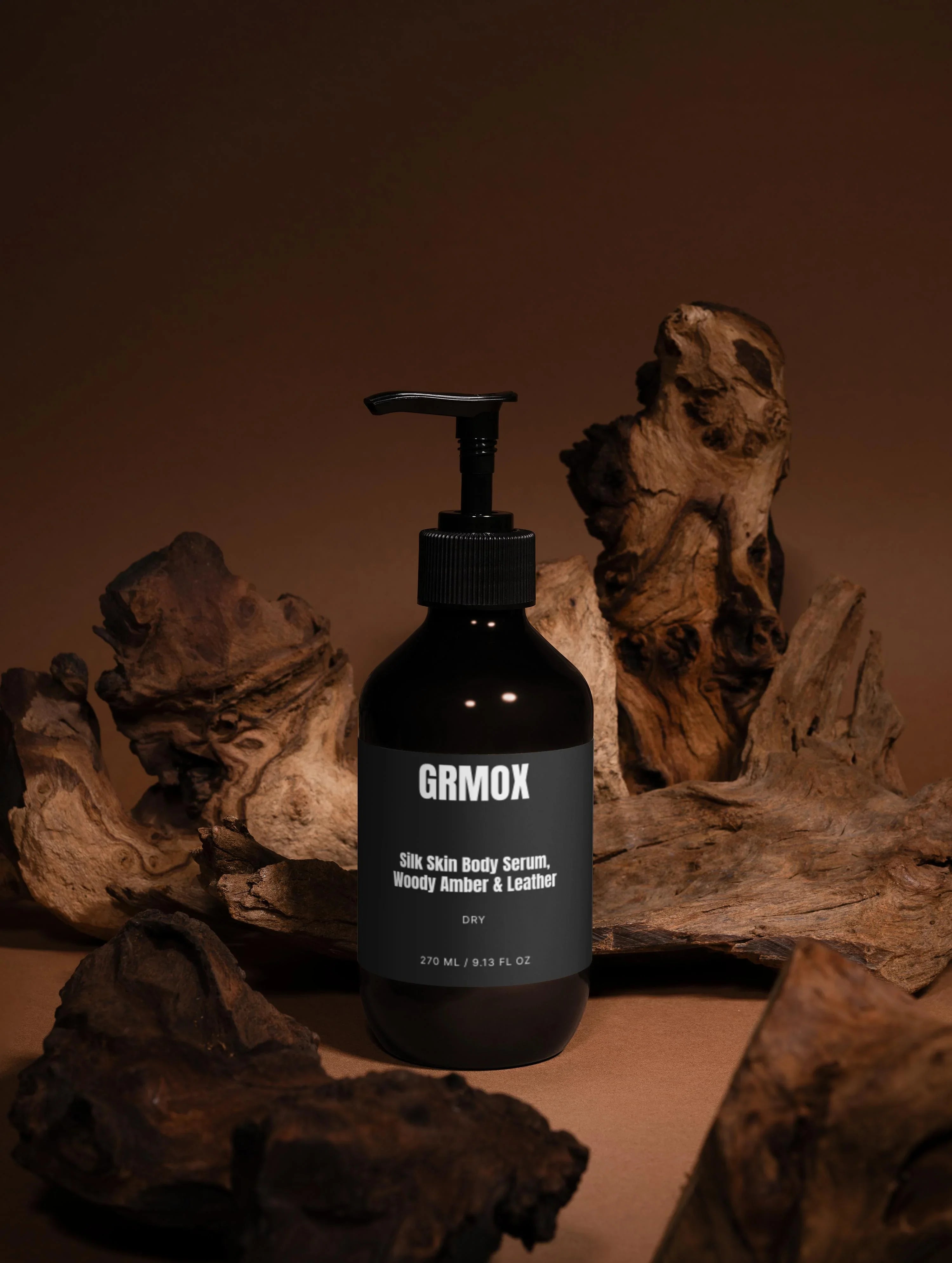 GRMOX Silk Skin Body Serum with Woody Amber & Leather scent, 270ml bottle on rustic driftwood