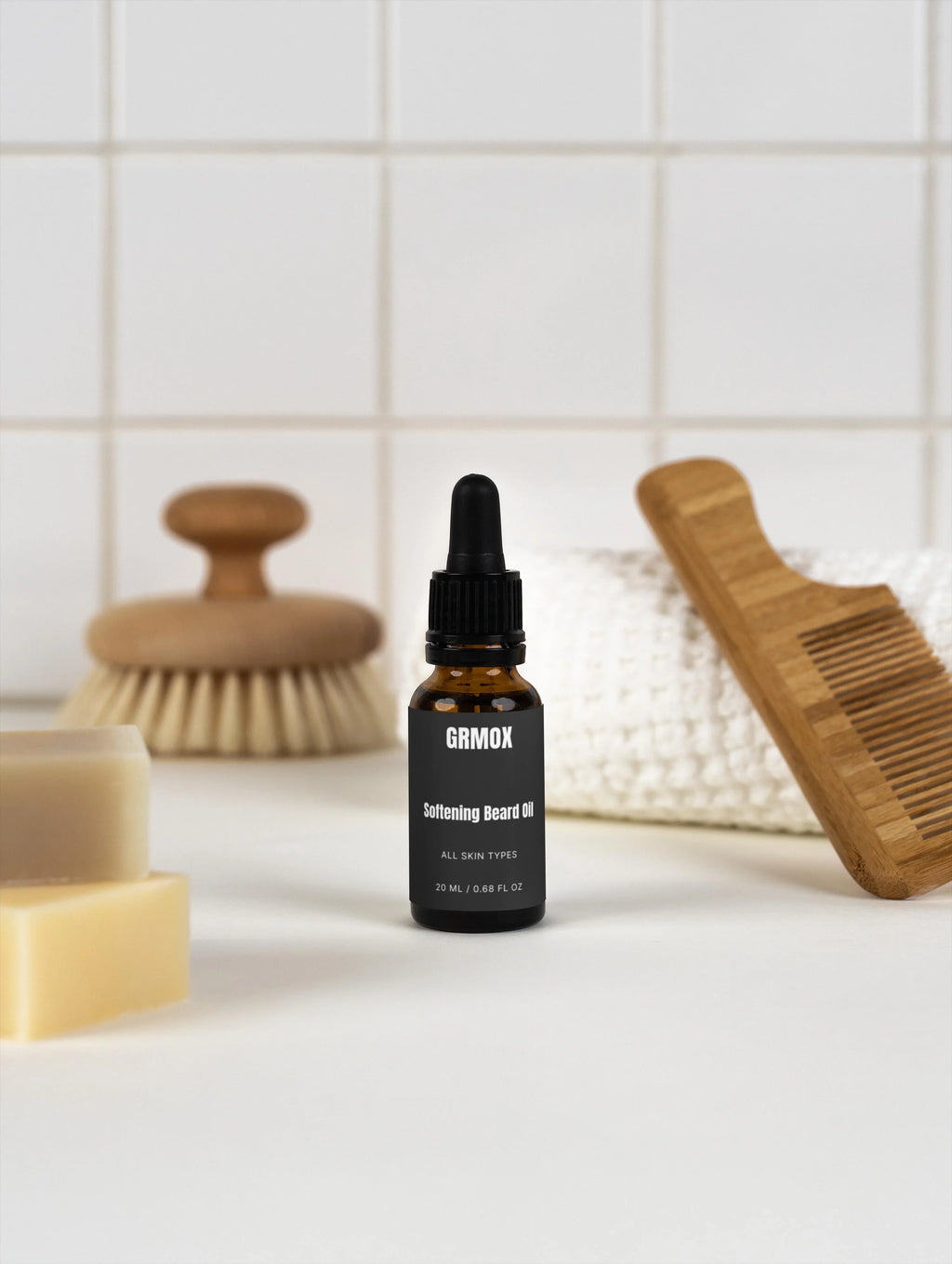 GRMOX Softening Beard Oil for all skin types, 20ml bottle with dropper, beside wooden comb and brush on white tile background