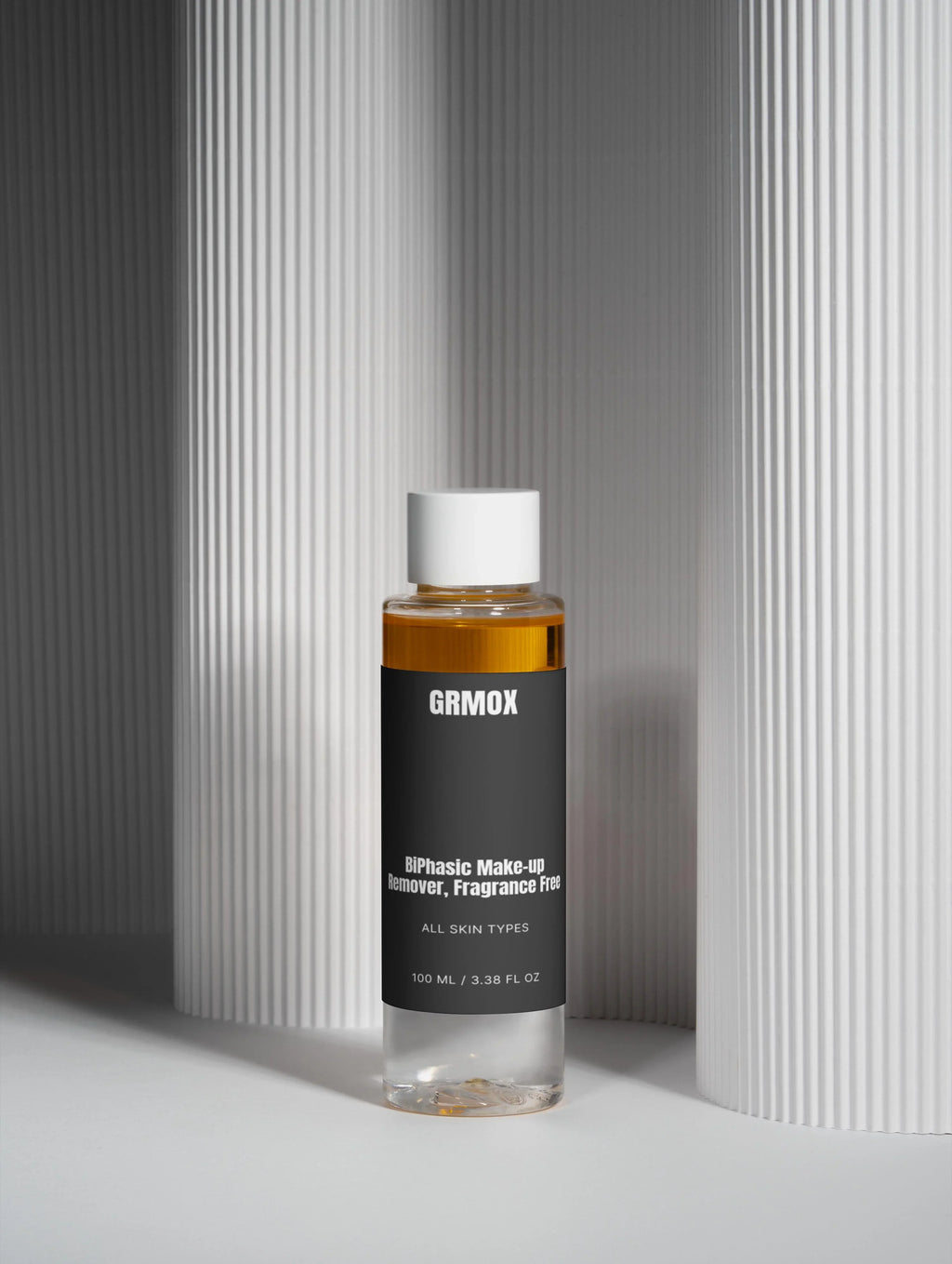 GRMOX biphasic makeup remover, fragrance-free for all skin types, 100ml bottle against textured white background