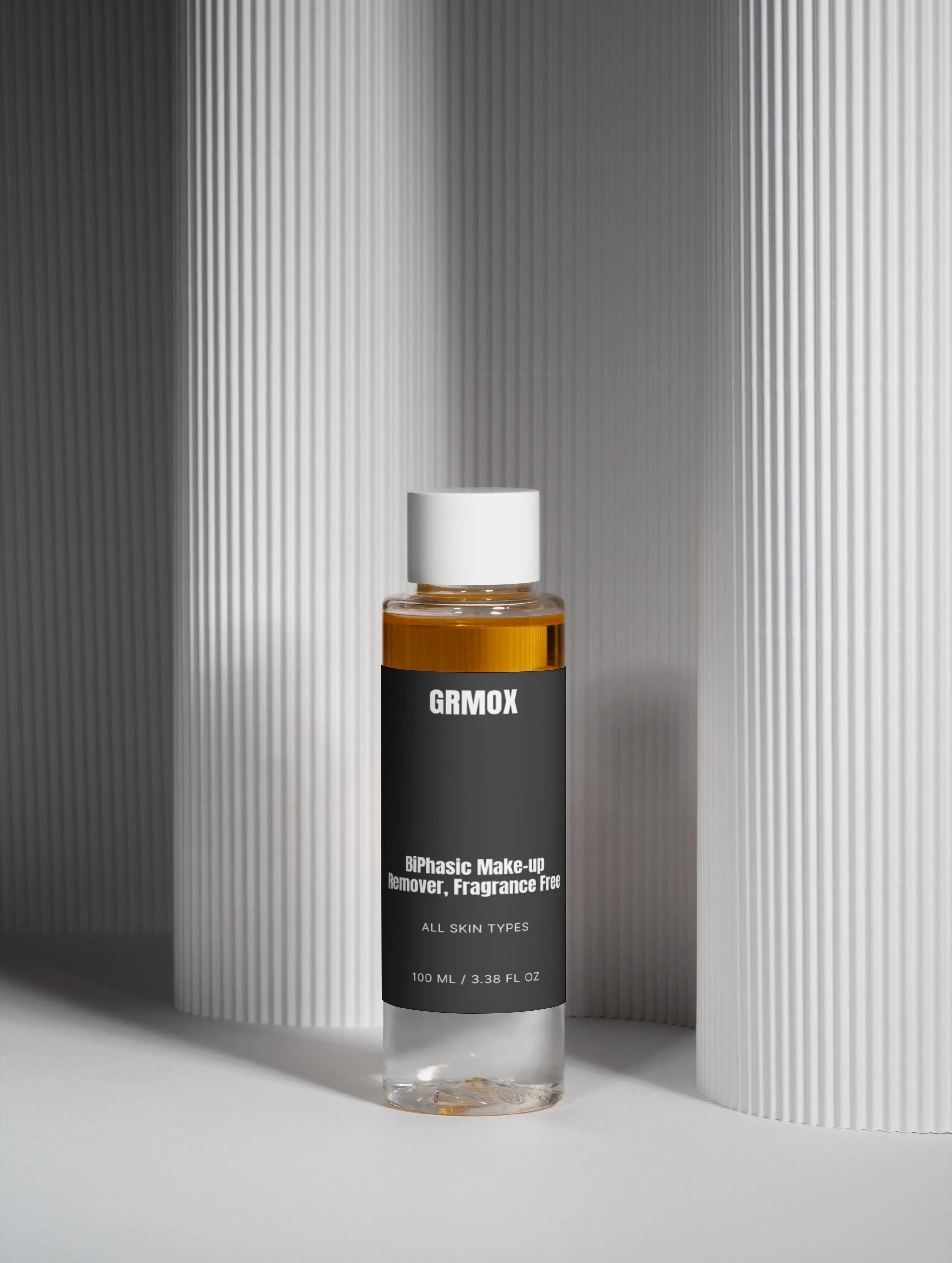 GRMOX biphasic makeup remover, fragrance-free for all skin types, 100ml bottle against textured white background