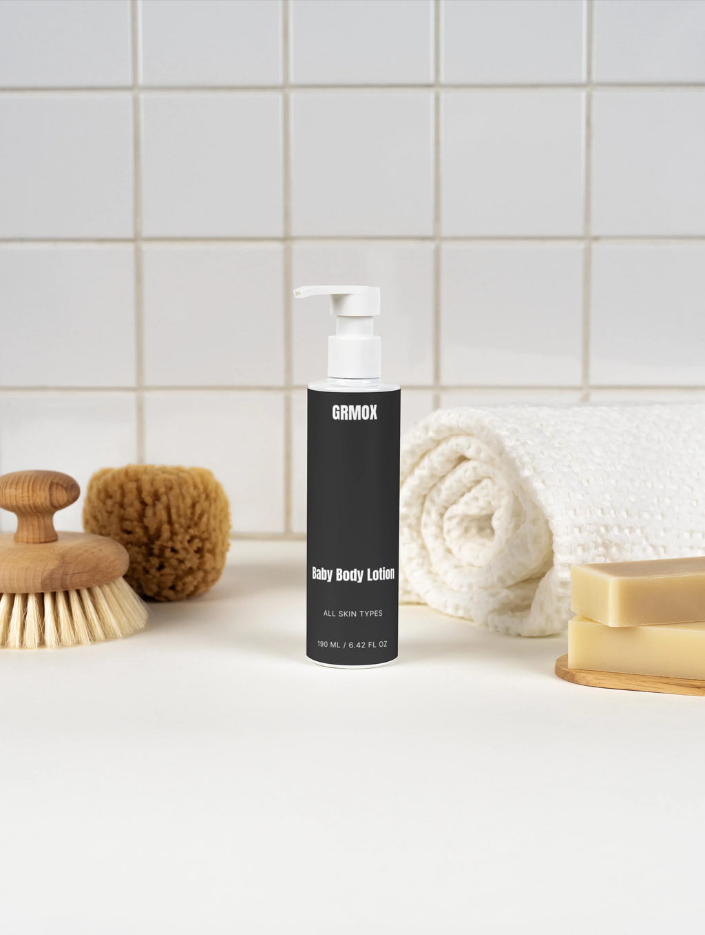 GRMOX Baby Body Lotion for all skin types, 190ml, with bath brush, towel, and soap bars on tiled bathroom counter