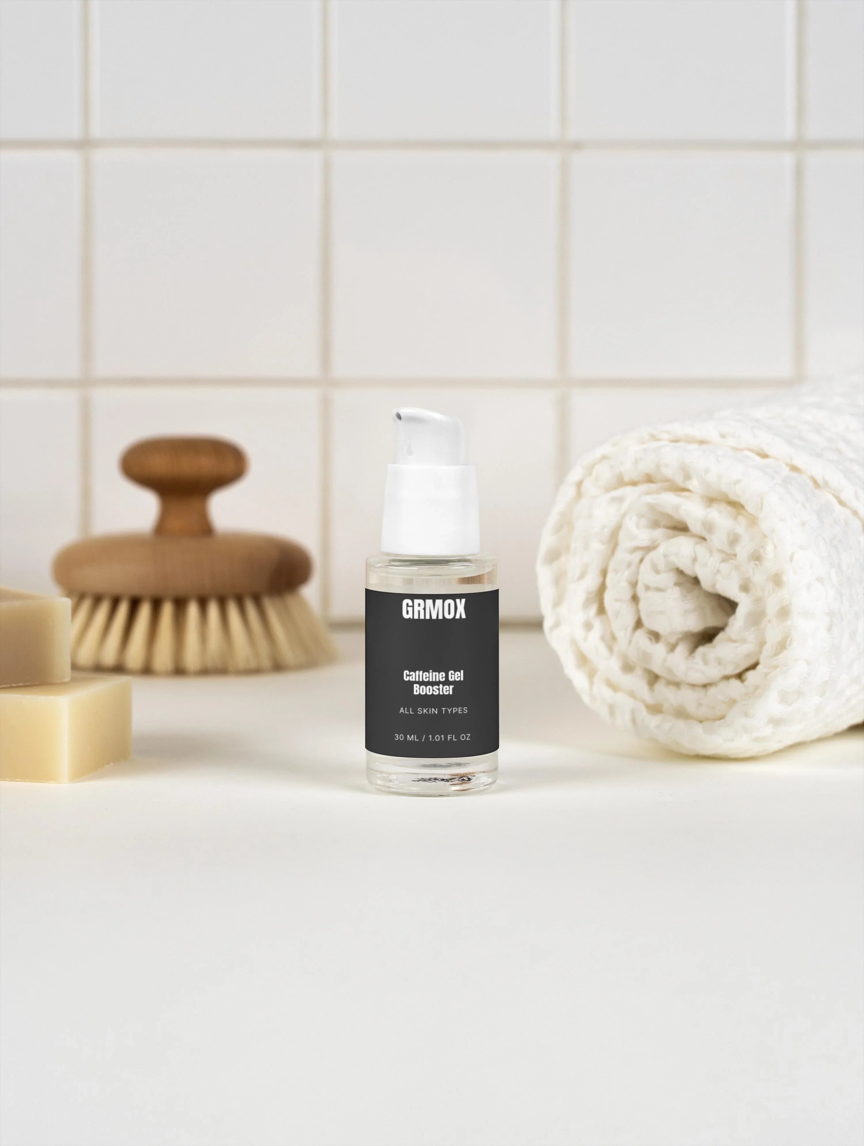 GRMOX Caffeine Gel Booster for all skin types, 30ml bottle with pump, beside towel and brush on white tile