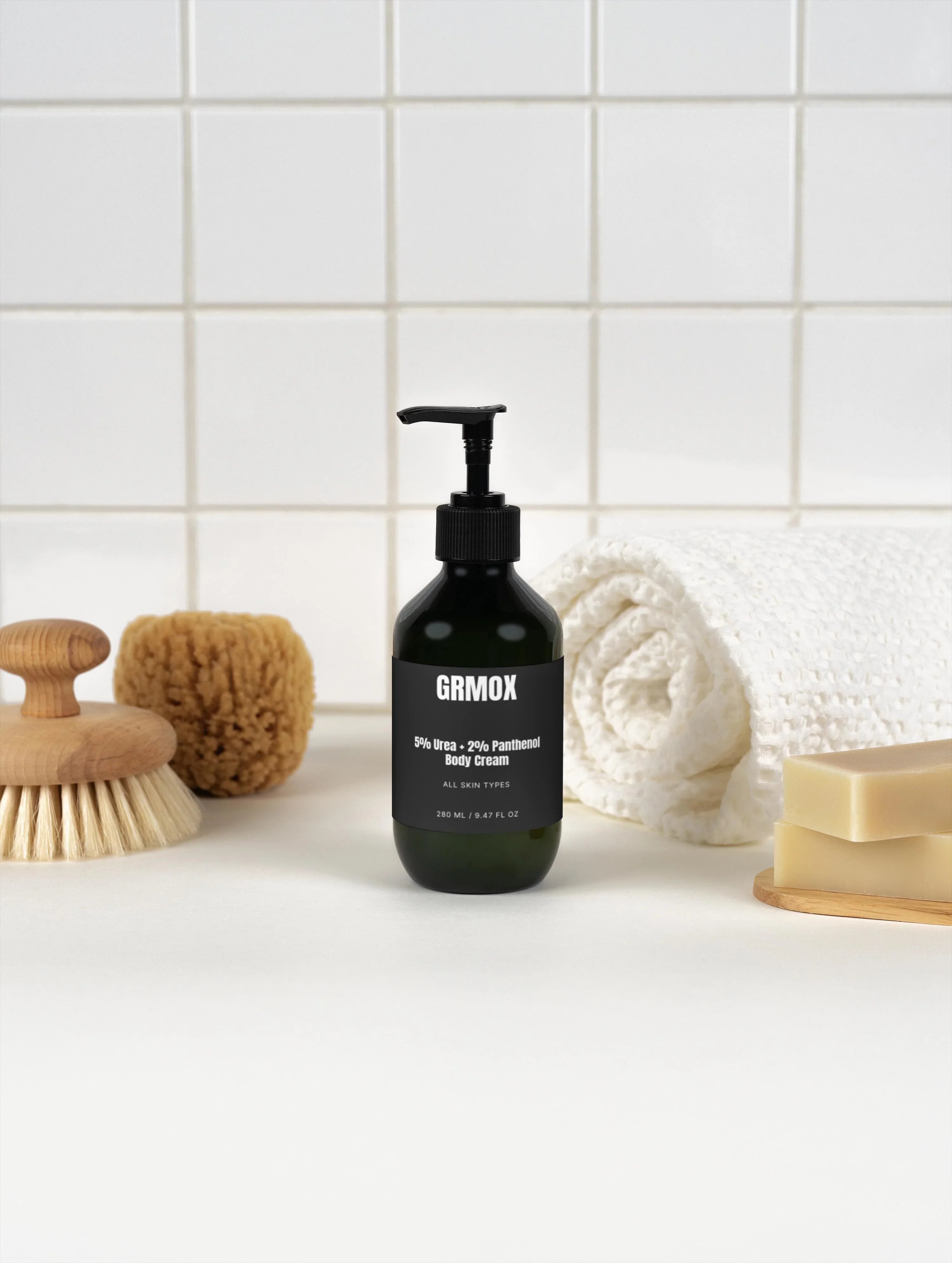 GRMOX 5% Urea + 2% Panthenol Body Cream for all skin types, shown with bath brush, towel, and soap on white tiles.