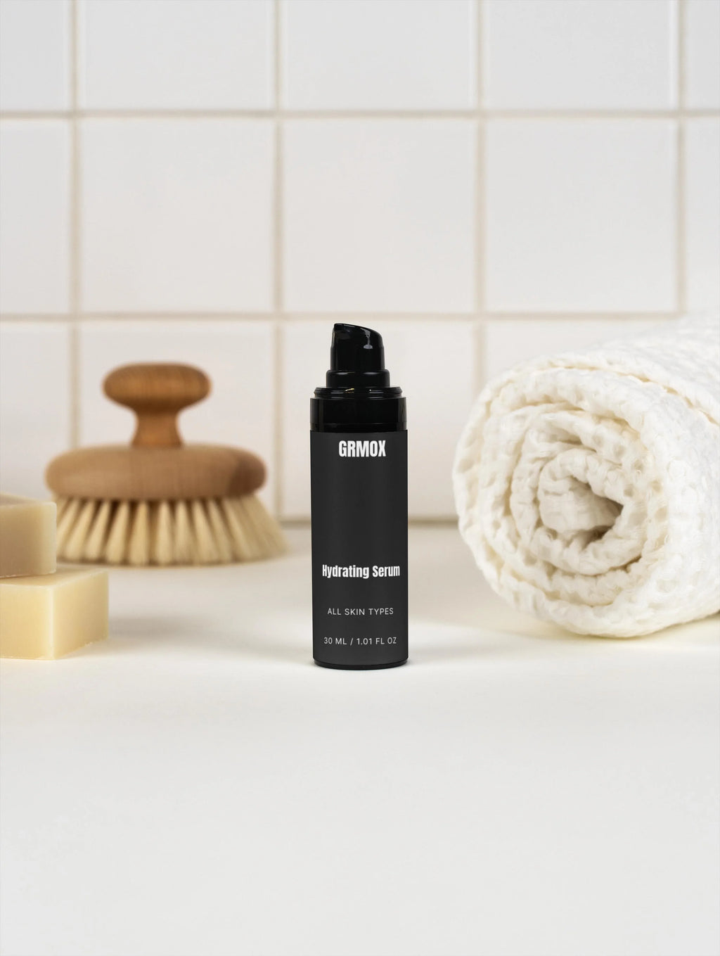 GRMOX Hydrating Serum for all skin types, 30ml bottle with pump, shown with bath brush and towel on tiled bathroom counter