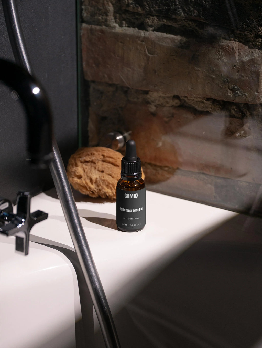 GRMOX Softening Beard Oil for all skin types, 20ml bottle on bathroom sink with natural sponge and stone wall background