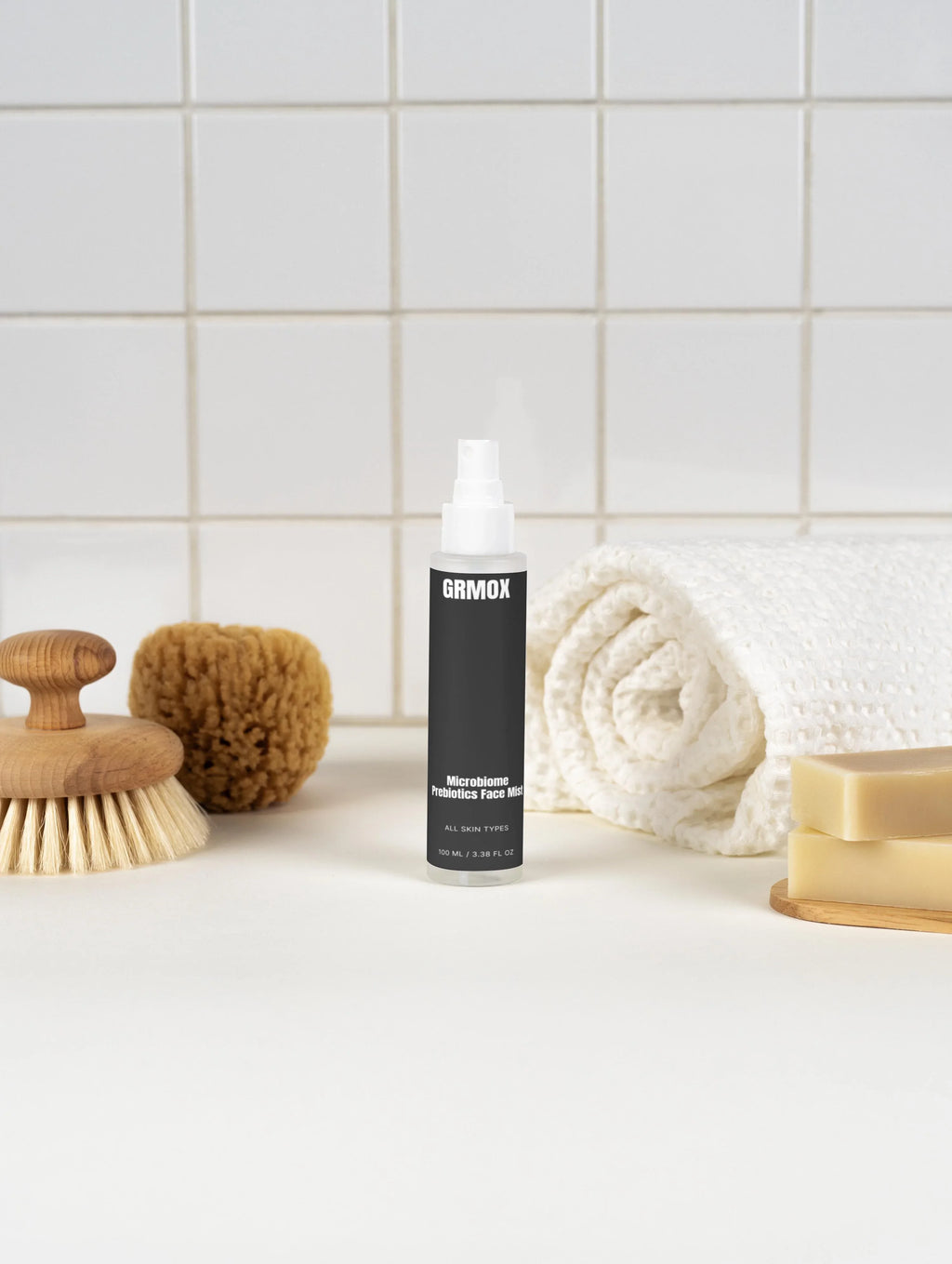 GRMOX Microbiome Prebiotics Face Mist for all skin types, shown with bath brush, sponge, towel, and soap on white tile background