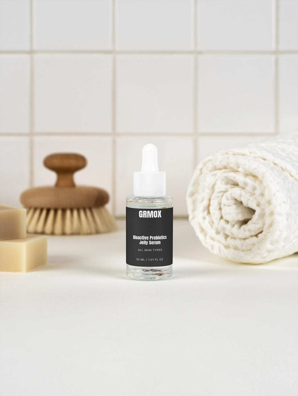 GRMOX Bioactive Prebiotics Jelly Serum for all skin types, 30ml, with dropper, beside towel and soap on tiled bathroom counter